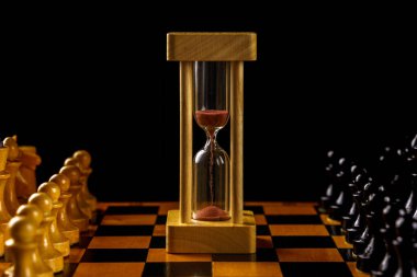 Hourglass in the center of the chessboard, black and white pieces. Soft focus, copyspace.