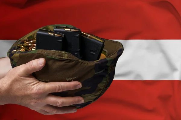 A military helmet with cartridges and magazines for a rifle in the hands of a man against the background of the flag of Austria. The concept of selling weapons or military assistance.