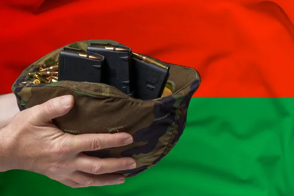 A military helmet with cartridges and magazines for a rifle in the hands of a man against the background of the flag of Burkina Faso. The concept of selling weapons or military assistance.
