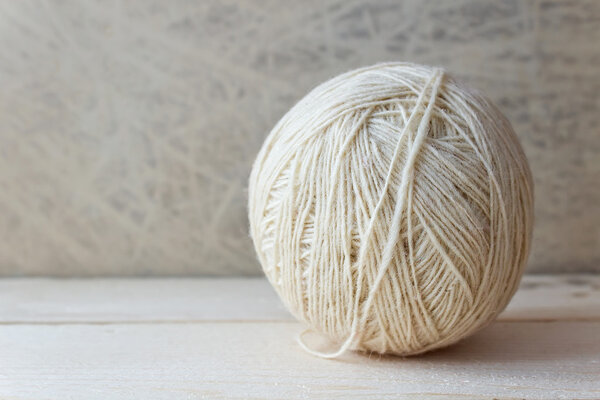 White ball of yarn on a wooden table over vintage wallpaper
