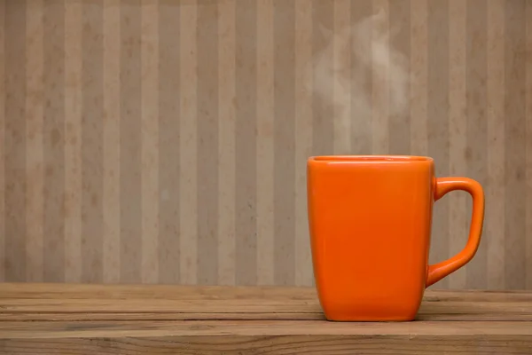 Orange mug on a wooden table over grunge wallpaper — Stock Photo, Image