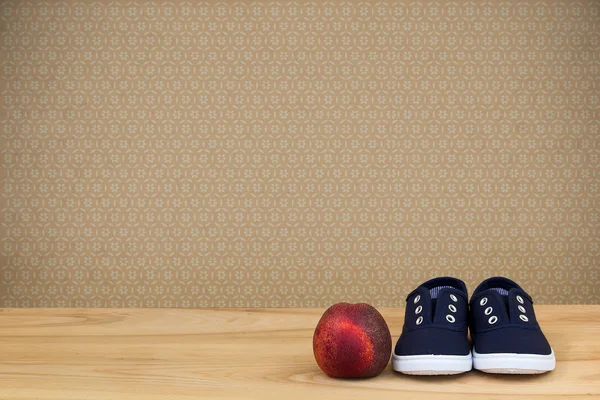 Sneakers and peach on wooden table over vintage wallpaper — Stock Photo, Image