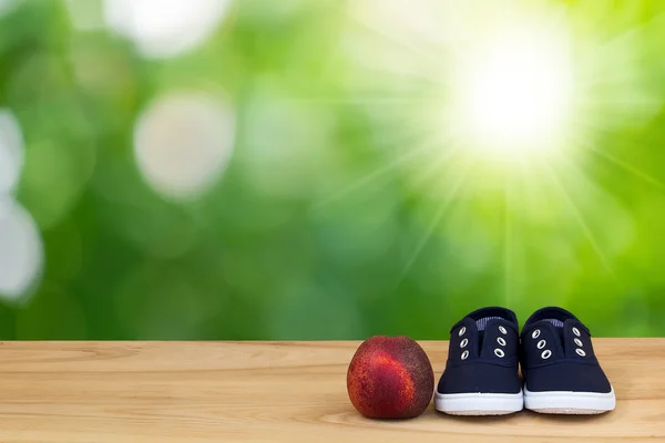 Sneakers and peach on foliage bokeh background — Stock Photo, Image