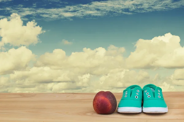 运动鞋和油桃在多云的天空木制的桌子上 — 图库照片