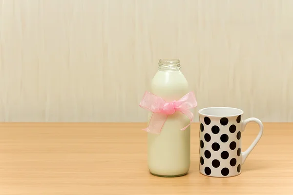 Jar of milk and a cup with dots on wooden table over wallpaper — Stock Photo, Image