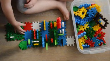 Küçük bir çocuk renkli parçalardan bir inşaat seti topluyor. Eller.