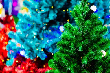 Ampullü yeşil Noel ağacı ve renkli Noel ağaçlarının bulanık odağı.