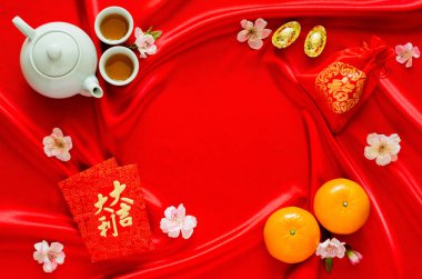 Red satin cloth background with tea set, ingots, red bag (word means wealth), oranges and red envelope packets or ang bao(word means auspice) for Chinese new year concept.