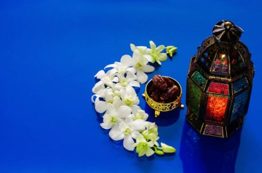 Mavi arka planda fener, orkide çiçeğinin üzerinde meyveler, kutsal Ramazan ayının Müslüman ziyafeti için hilal şeklinde ayarlanmış..