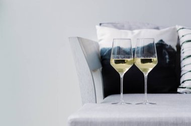 Beyaz duvarlı arka planı olan bir çifti kutlamak için iki kadeh beyaz şarap ve yastıklı kanepe..