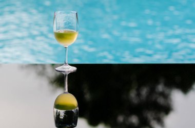 A glass of white wine puts on table at swimming pool for Holiday and summer drink concept.