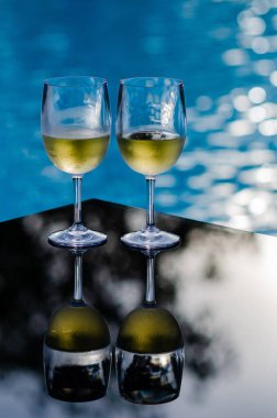 Tatil ve yaz içkisi konsepti için yüzme havuzunda masaya iki bardak beyaz şarap..