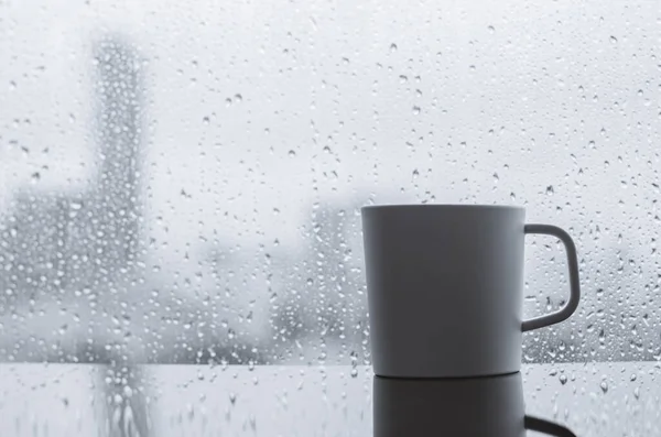 A cup of coffee puts on table in morning with rain drop on window. Stay home and relaxing concept.