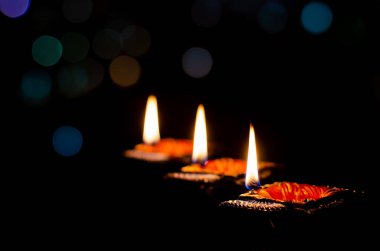 Selective focus on flame of clay diya lamps lit on dark background with colorful bokeh lights. Diwali festival concept.