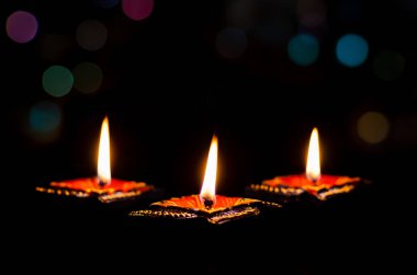 Selective focus on flame of first clay diya lamps lit on dark background with colorful bokeh lights. Diwali festival concept.