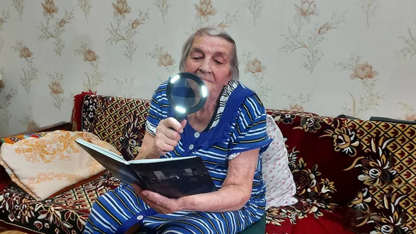 Uma mulher idosa lê através de uma grande lupa Fotografia De Stock