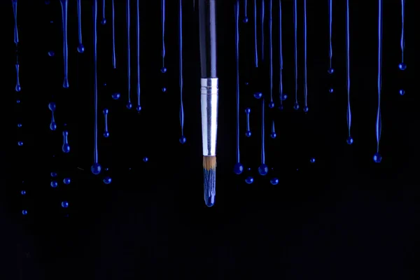 Mavi boya siyah arka planda fırçanın etrafına damlıyor.