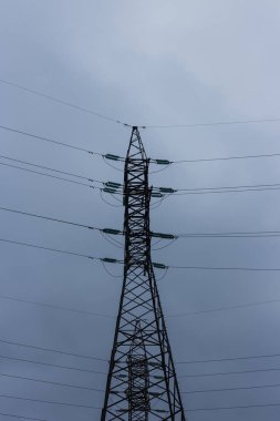 Bulutlu gökyüzünün arka planında elektrik hatları.