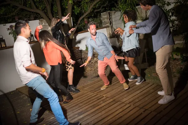 Neşeli erkekler ve kadınlar arka bahçede dans ediyor.