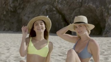 Kumsalda oturup kameraya bakan mutlu kızlar.