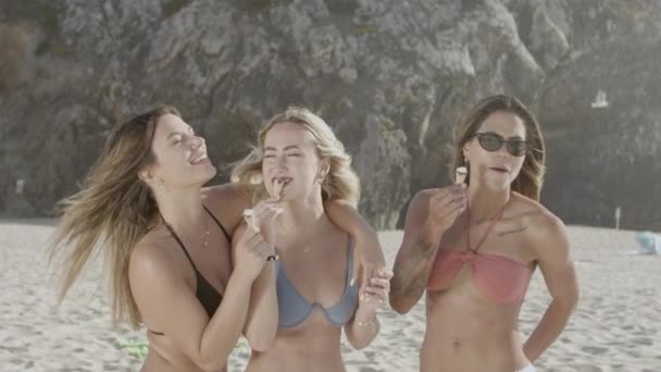 Donne in bikini in piedi sulla spiaggia e mangiare gelato — Video Stock