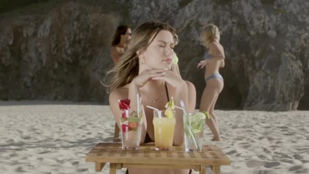Happy girl siedzi na plaży z rękami na stole z zimnymi napojami — Wideo stockowe