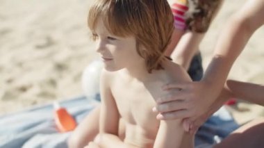 Yavaş çekimde ablaların elleri erkeklere güneş kremi sürüyor.