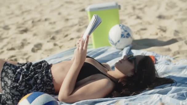 Hermosa chica caucásica acostada en la playa y leyendo libro — Vídeo de stock