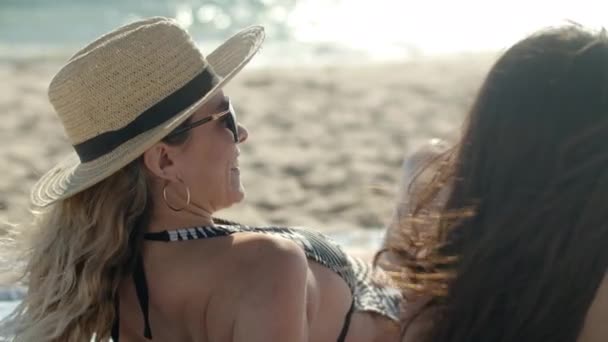 Visão traseira da mulher de chapéu banhos de sol na praia de areia com amigo — Vídeo de Stock