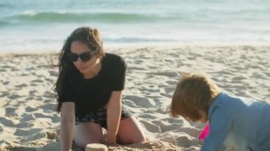 Odaklanmış kız kardeşler ve küçük kardeş kumsalda kumdan kale yapıyorlar.