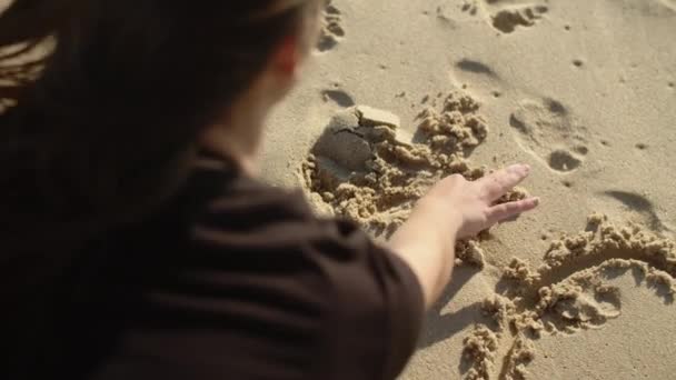 Widok z tyłu dziewczyna rysunek gwiazda w mokrym piasku na plaży — Wideo stockowe