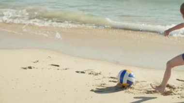 Küçük çocuğun topa vurup kıyı şeridinde koşarkenki görüntüsü.