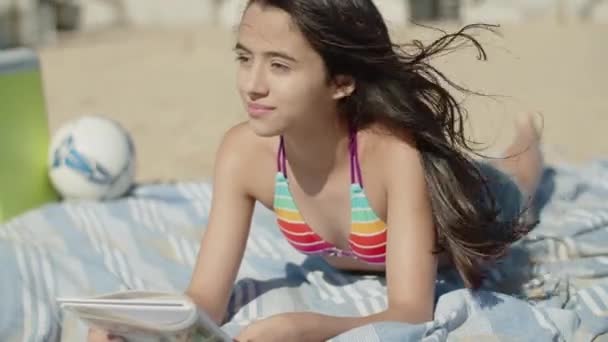 Movimento vertical de adolescente do sexo feminino que coloca na praia com livro — Vídeo de Stock