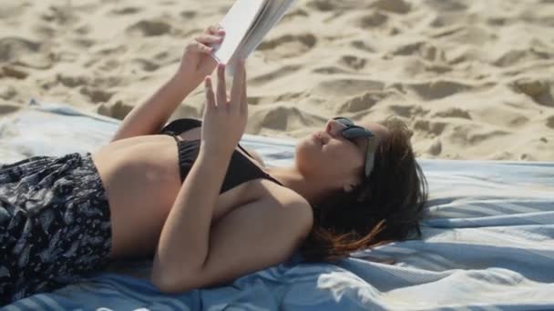 Średni strzał młodej uroczej kobiety leżącej na plaży i czytającej książkę — Wideo stockowe