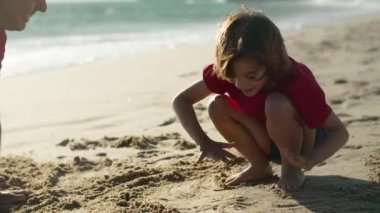 Mutlu baba ve oğlunun kumsalda el izi yaptığı orta boy bir fotoğraf. 