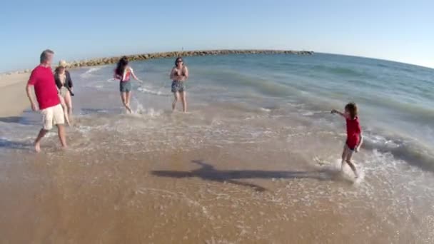 Largo tiro de familia feliz salpicando el agua en la playa — Vídeos de Stock