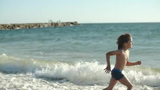 Vista lateral del niño feliz corriendo y saltando a lo largo de la costa — Vídeos de Stock