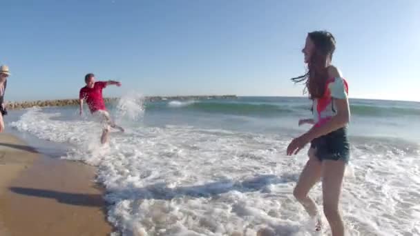 Colpo lungo di sorelle felici che spruzzano acqua sui genitori sulla spiaggia — Video Stock