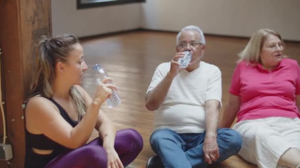 Ηλικιωμένοι που κάθονται στο πάτωμα στην αίθουσα χορού με τον δάσκαλο χορού — Αρχείο Βίντεο