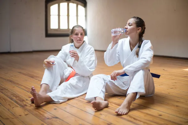 Yorgun beyaz karateci kızlar yerde su içiyor.