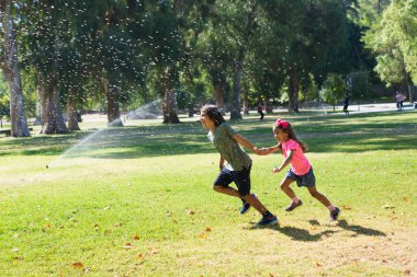 Neşeli kız ve erkek kardeş su sıçratarak oynuyorlar.