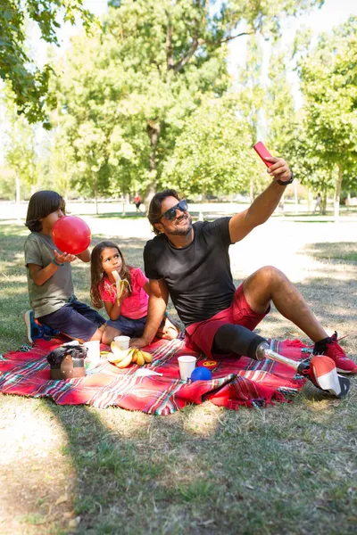 Отец с ограниченными возможностями делает селфи с детьми на пикнике — стоковое фото