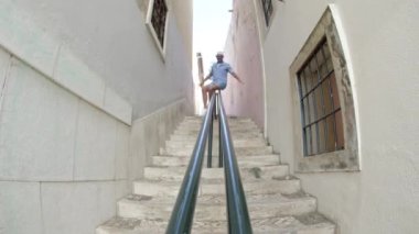 Dar bir sokakta merdivenlerden kayan bir adamın uzun bir görüntüsü.