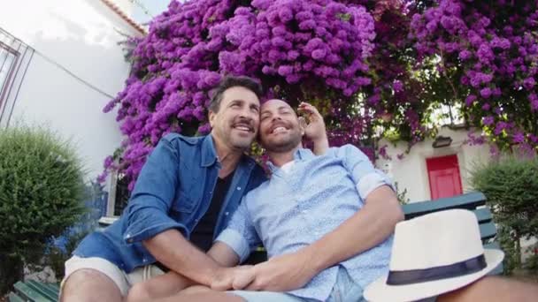 Widok z przodu geje całowanie na ławce w parku z kwitnących drzew — Wideo stockowe