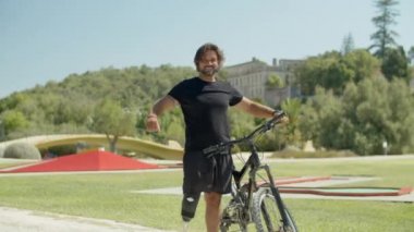 Biyonik bacağı olan mutlu bisikletçi zafer işareti olarak el kaldırıyor.