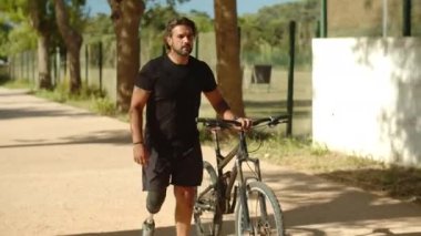 Özürlü neşeli bir adam yol boyunca gidiyor ve bisikleti yuvarlıyor.