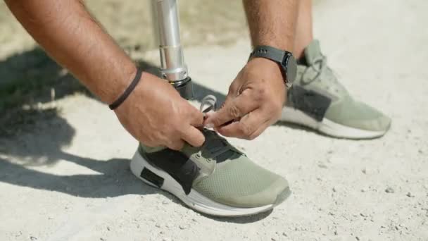 Крупним планом чоловік з біонічною ногою зав'язуючи шнурки на спортивне взуття — стокове відео