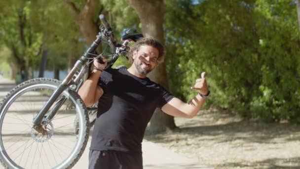 Homem com deficiência levantando bicicleta e mostrando sinal de shaka — Vídeo de Stock