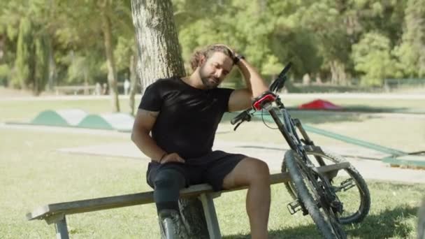 Κουρασμένος άνθρωπος με τεχνητό πόδι κάθεται στον πάγκο μετά την ποδηλασία — Αρχείο Βίντεο