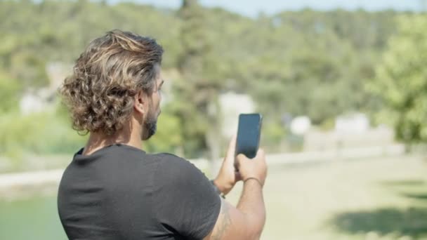 Вид ззаду людини, що фотографує краєвид під час їзди на велосипеді в парку — стокове відео
